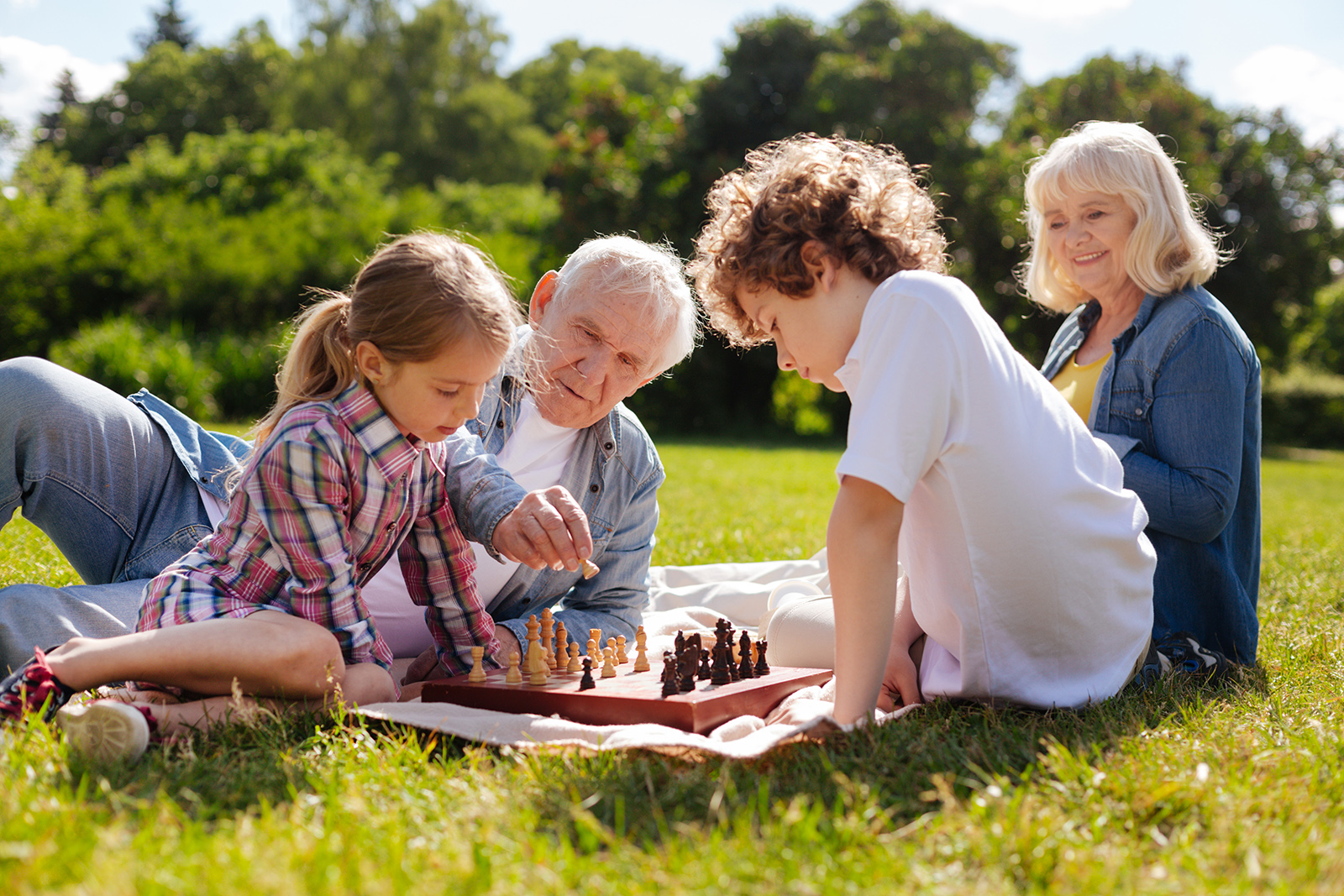Grandparents sitting in the grass playing chess with their grandchildren