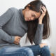 young woman sitting on the bed feeling pain in stomach
